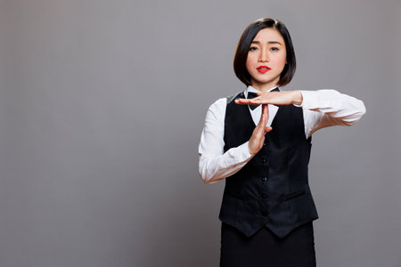Serious asian waitress showing time out gesture with hands and looking at camera with confident facial expression. Young attractive woman receptionist making interruption symbol portraitの写真素材