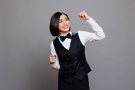 Cheerful asian waitress dressed in restaurant uniform dancing with joyful facial expression. Cafe smiling woman employee making moves with hands and body, spreading happinessの写真素材