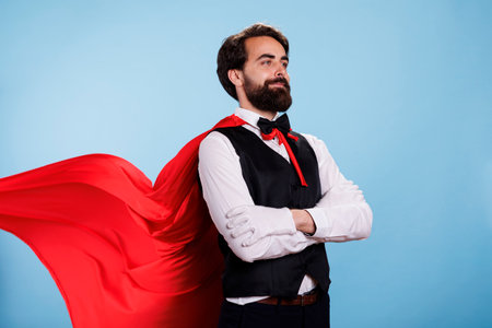 Person wearing red cape and formal suit posing with confidence, feeling determined to help and save people. Young man pretending to be fantasy cartoon superhero with mantle, superhuman.の写真素材
