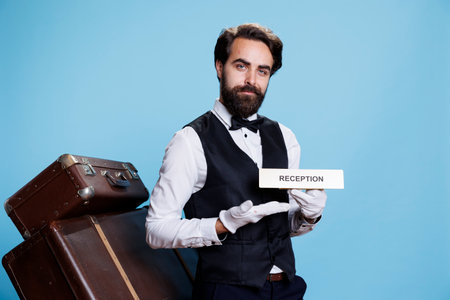 Doorman poses with sign of reception that guides persons to the hotel lobby area. Experienced staff member in the tourism industry using the entrance front desk symbol indicator.の写真素材
