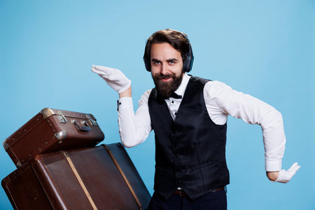 Hotel concierge dances in studio, having fun with songs on deaset while he wears professional suit and tie. Doorkeeper employee enjoying music on headphones, feeling pleased.の写真素材