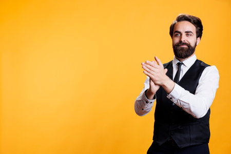 Smiling butler clapping hands in studio, feeling cheerful after congratulating person for success. Young adult with waiter profession applauding and cheering for someone, confidence boost.の写真素材
