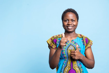 African american woman showing thumbs up sign and smiling at camera, presenting agreement on something and feeling pleased. Positive joyful adult gives like and shows approval with good symbol.の写真素材