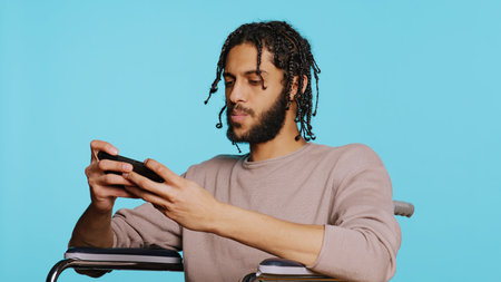 Joyful person in wheelchair playing videogames on smartphone, having positive burst of emotion after defeating opponents. Ecstatic gamer winning game on phone, studio background, camera Bの写真素材