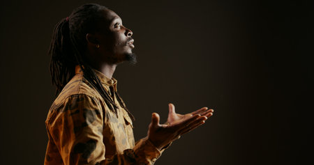 Spiritual person believing in God and praying on camera, showing belief and being hopeful over black background. Religious adult feeling optimistic and talking to Jesus. Handheld shot. Close up.の写真素材