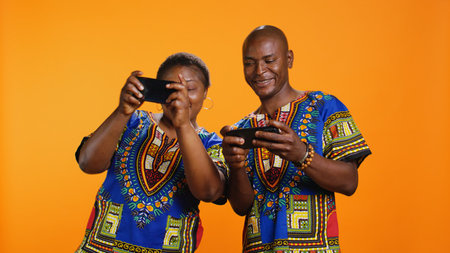 African american people playing videogames on mobile device, having fun with online gaming contest in studio. Married man and woman enjoying game tournament on smartphone app.の写真素材