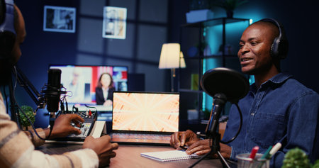 African american influencer recording podcast with man, talking in studio. Zoom in shot of cheerful man listening to guest live during broadcasting session for internet showの写真素材