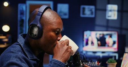 African american show host recording podcast with guest, using analog mixer and professional mic in studio. Close up shot of man setting up audio devices for live broadcast for flawless sound qualityの写真素材