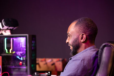 Gamer laughing at home, having fun playing videogames on computer. Joyous african american man contending in gaming tournament using powerful neon lit desktop PC in apartmentの写真素材