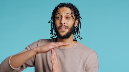 Assertive Middle Eastern man asking for timeout, doing hand gestures. BIPOC man doing pause sign gesturing, wishing for break, isolated over blue studio background, camera Bの写真素材