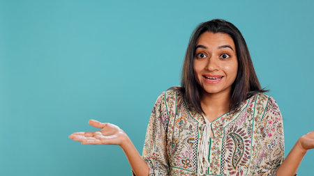 Indian woman shrugging shoulders, unable to provide answer, having detached apathy facial expression. Apathetic person doing hand gesturing showing lack of knowledge, studio background, camera Bの写真素材