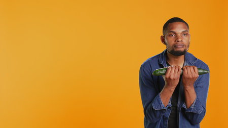Confident person pretending to do workout exercises with a cucumber, lifting weight by using a fresh homegrown vegetable. Playful person advocating vegan nutrition and zero waste. Camera B.の写真素材