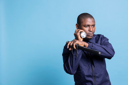 African american guard going on a patrol at night with flashlight and baton for safety, control sweep in the dark. Professional agent using a lantern to examine the premises for protection.の写真素材