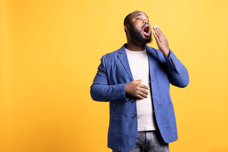 African american man feeling exhausted and yawning, covering his mouth, isolated over studio background. BIPOC person being sleepy during morning, awaken too early, showing sleepinessの写真素材