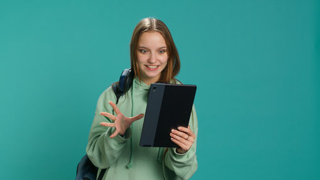 Radiant woman having funny conversation with friends during online teleconference using tablet, studio background. Upbeat girl having fun with mates during internet videocall on device, camera Aの写真素材