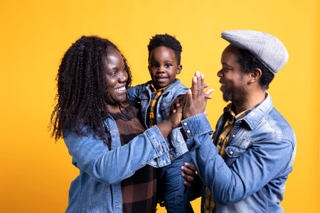 Happy black family sharing a high five together in the studio, feeling cheerful and showing affection to each other. African american couple with a small toddler posing with gratitude.の写真素材