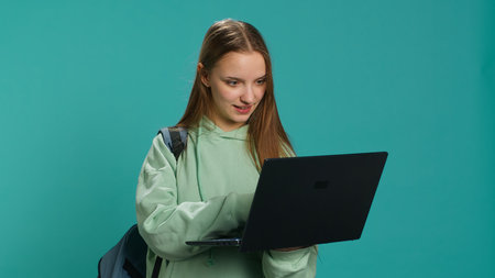 Joyful woman adding payment method on website using laptop, enjoying sales period, studio background. Girl doing purchases on internet, typing credit card information on notebook, camera Aの写真素材