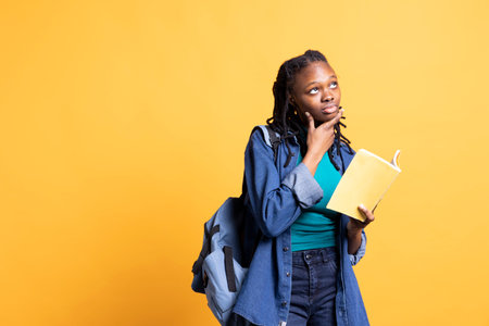 Portrait of BIPOC woman daydreaming while holding book, thinking of characters. Person with novel in arms caught in imagination while enjoying leisure time, isolated over studio backgroundの写真素材