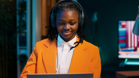 Student listening to music while she writes her essays at home, enjoying groovy tunes on headphones. Young woman creating a relaxing atmosphere to finish homework and tasks. Camera A.の写真素材