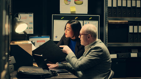 Team members discuss theories while reading past investigations cases to find connections, gathering similar information from old crimes. Law officers collaborating in the archive room. Camera A.の写真素材