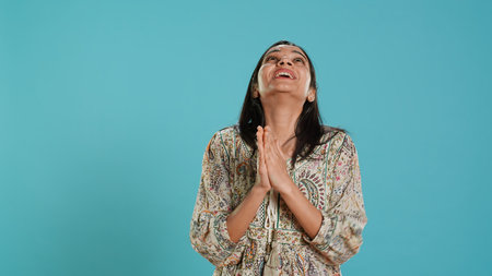 Indian woman putting hands together in begging gesture, making wish, isolated over studio background. Faithful person looking upwards to sky, asking for something, praying and hoping, camera Aの写真素材