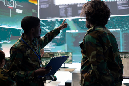 Servicemen working on new national safety plan for an operation, studying the CCTV surveillance system together in military control room. Military personnel analyze satellite support.の写真素材