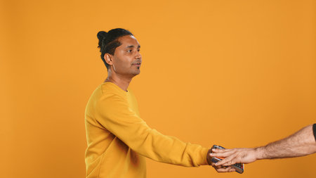 Friendly upbeat pizza delivery employee giving takeaway order to client paying with credit card. Asian man offering food order and digital payment method to customer, studio background, camera Aの写真素材