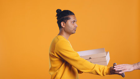 Portrait of indian pizza delivery man taking takeaway orders out of thermal backpack. Upbeat courier removing lunch boxes from transportation bag, isolated over studio background, camera Bの写真素材
