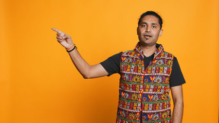 Salesman pointing around with finger, doing recommendation, talking with audience. Indian person showing copy text, doing advertisement, isolated over studio background, camera Bの写真素材