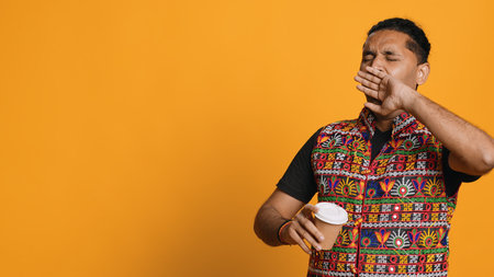 Sleepy man yawning and rubbing eyes. sipping coffee to wake up and gain energy. Exhausted person feeling fatigued after sleepless night, drinking caffeinated beverage, studio backdrop, camera Aの写真素材