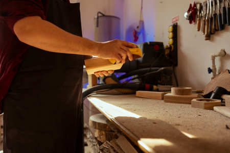 Woodworker in carpentry shop using sandpaper for sanding wooden surface before painting it, ensuring adequate finish. Woodworking specialist using abrasive sponge to fix damages suffered by woodの写真素材
