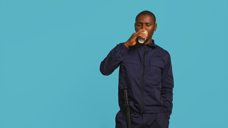 Portrait of security agent uses coffee cup to remain energized while securing assigned post, studio background. Guardian consuming caffeinated beverage to be able to handle security breaches, camera Bの写真素材