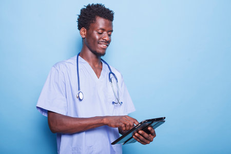 Black doctor with a smile and stethoscope is researching healthcare on tablet. African American physician using his digital gadget to browse the internet while standing in the studio.の写真素材