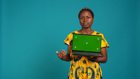 Confident happy person posing with a copy space mockup on laptop, create an advertisement with isolated display in studio. Young woman in ethnic attire with floral elements. Camera B.の写真素材