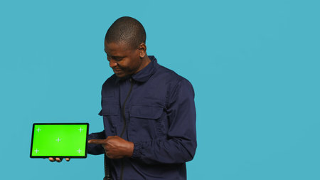 Portrait of security agent presenting chroma key tablet and securing assigned post, studio background. Guardian points finger to isolated screen device while handling security breaches, camera Aの写真素材