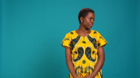 Young natural woman looking both left and right sides in studio, checking the environment and her surroundings. Casual girl wears traditional african attire with tribal native pattern. Camera B.の写真素材