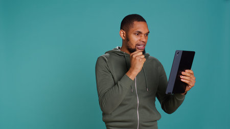 Angry man fighting with friend during videocall on tablet, isolated over studio background. Rude person in disagreement with mate, swearing and pointing finger in teleconference meeting, camera Bの写真素材