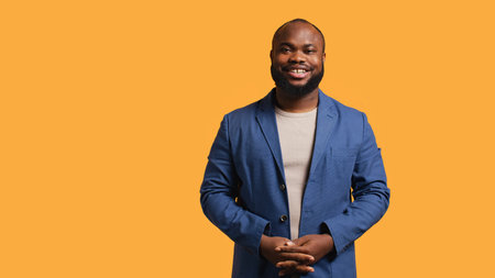 Portrait of cheerful african american man smiling, looking pleased, isolated over yellow studio background. Happy expressive BIPOC person stylishly dressed grinning, feeling satisfied, camera Bの写真素材