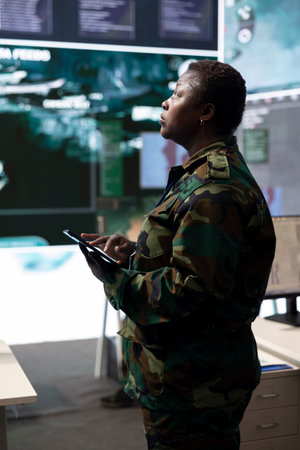 Woman trooper analyzing crucial battlefield data on a big screen in military control center, base of operations. Female engineer collecting and comparing information, reconnaissance.の写真素材