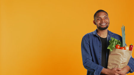 Portrait of cheerful guy pleased with homegrown groceries in a paper bag, feeling happy with his freshly harvested goods to support sustainable lifestyle. Vegan nutrition healthy eating. Camera B.の写真素材