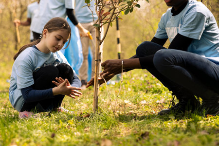 Young girls activists collaborate to plant more trees in the woods, covering holes and increasing vegetation. Child and teenager doing voluntary work to protect the forest ecosystem.の写真素材