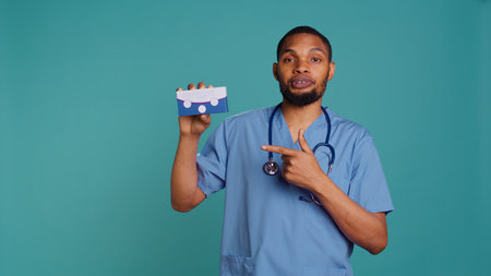 Portrait of medic in scrubs holding medicine package for patients suffering from illnesses, studio backdrop. Hospital staff member recommending tablets for patients with chronic diseases, camera Bの写真素材