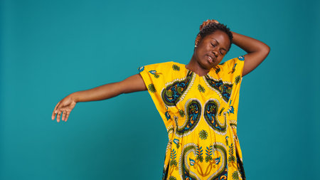 Sleepy cute young woman yawning in studio and feeling overworked, dealing with sleep deprivation and being exhausted. Tired girl dressed in african native traditional clothes, sleepiness. Camera B.の写真素材