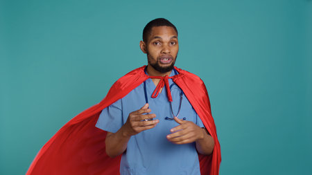 Male nurse portraying superhero showing courage and strength fighting diseases, studio backdrop. Portrait of african american doctor posing as hero in costume, holding empowering speech, camera Bの写真素材