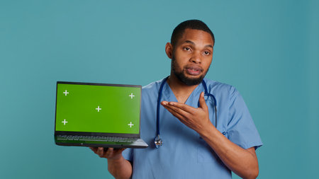 Portrait of african american medic in protective medical uniform using green screen laptop. Healthcare specialist doing presentation using mockup notebook, showing patient treatment plan, camera Aの写真素材