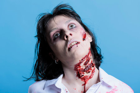 Woman with bloody neck pretending to be dead before turning into zombie, filming horror film scene. Actress acting as undead corpse with professional SFX makeup scars, studio backgroundの写真素材