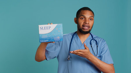 Portrait of african american medic holding sleep deprivation medicine package for insomniacs, studio background. Healthcare specialist recommending tablets for patients with insomnia, camera Aの写真素材