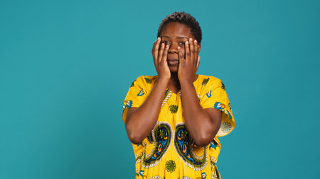 Horrified young woman covering her eyes to avoid seeing something, feeling squeamish and appalled about a thing in studio. Being disgusted and shocked in ethnic clothing. Camera A.の写真素材