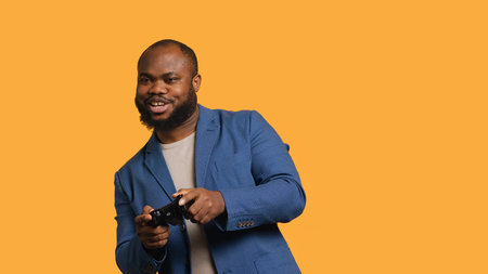 Cheerful african american gamer showing thumbs up sign gesturing holding controller, playing videogames. Joyful person excited to do gaming, doing approving hand gesture, studio background, camera Aの写真素材
