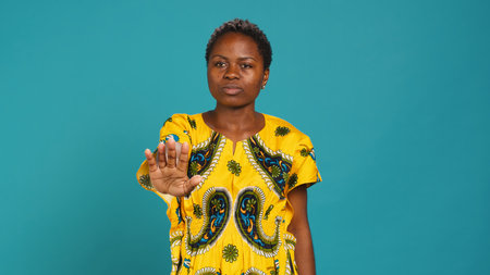 Displeased irritated woman raising her palm and saying no, showing a stop sign against blue background. Young dissatisfied person presenting a negative reaction, refusal. Camera A.の写真素材